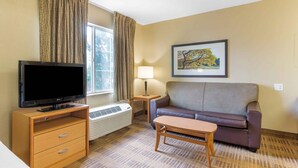 Een hotelkamer met een televisie, bank, tafel, lamp en een lijstje aan de muur.