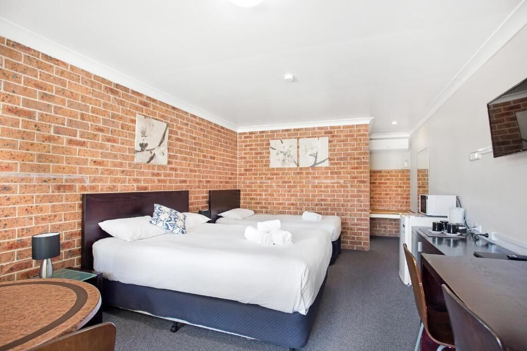 A hotel room with a brick wall, two beds, a desk, and a flat-screen TV.