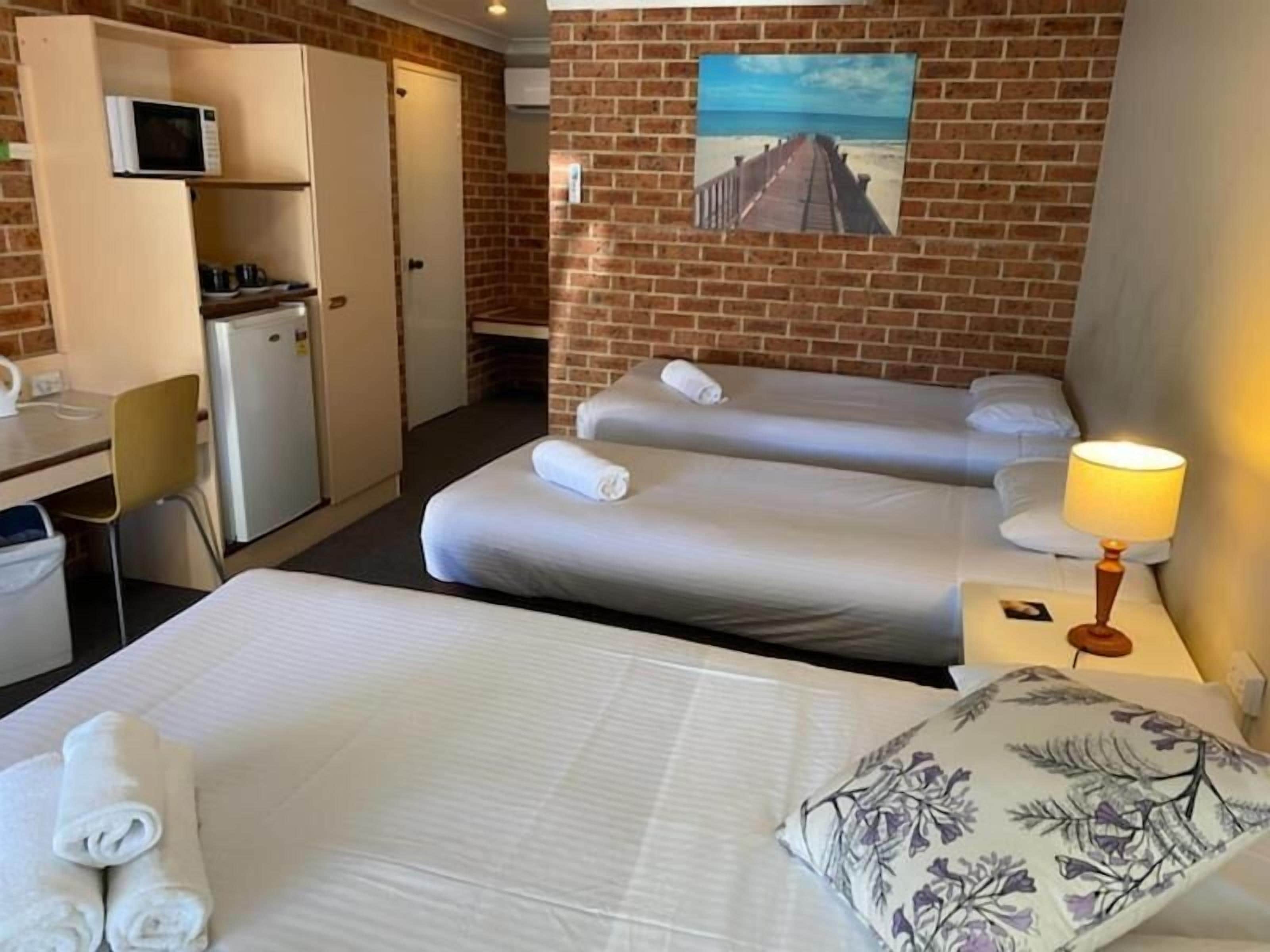 A hotel room with two beds, a desk, a refrigerator, and a painting on the wall.