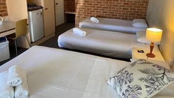 A hotel room with two beds, a desk, a refrigerator, and a painting on the wall.