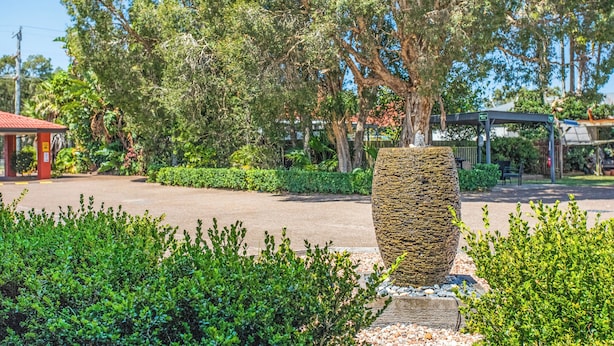A stone planter in a landscaped area with a paved path and a gazebo in the background. - Lake Macquarie Motor Inn (Marks Point)