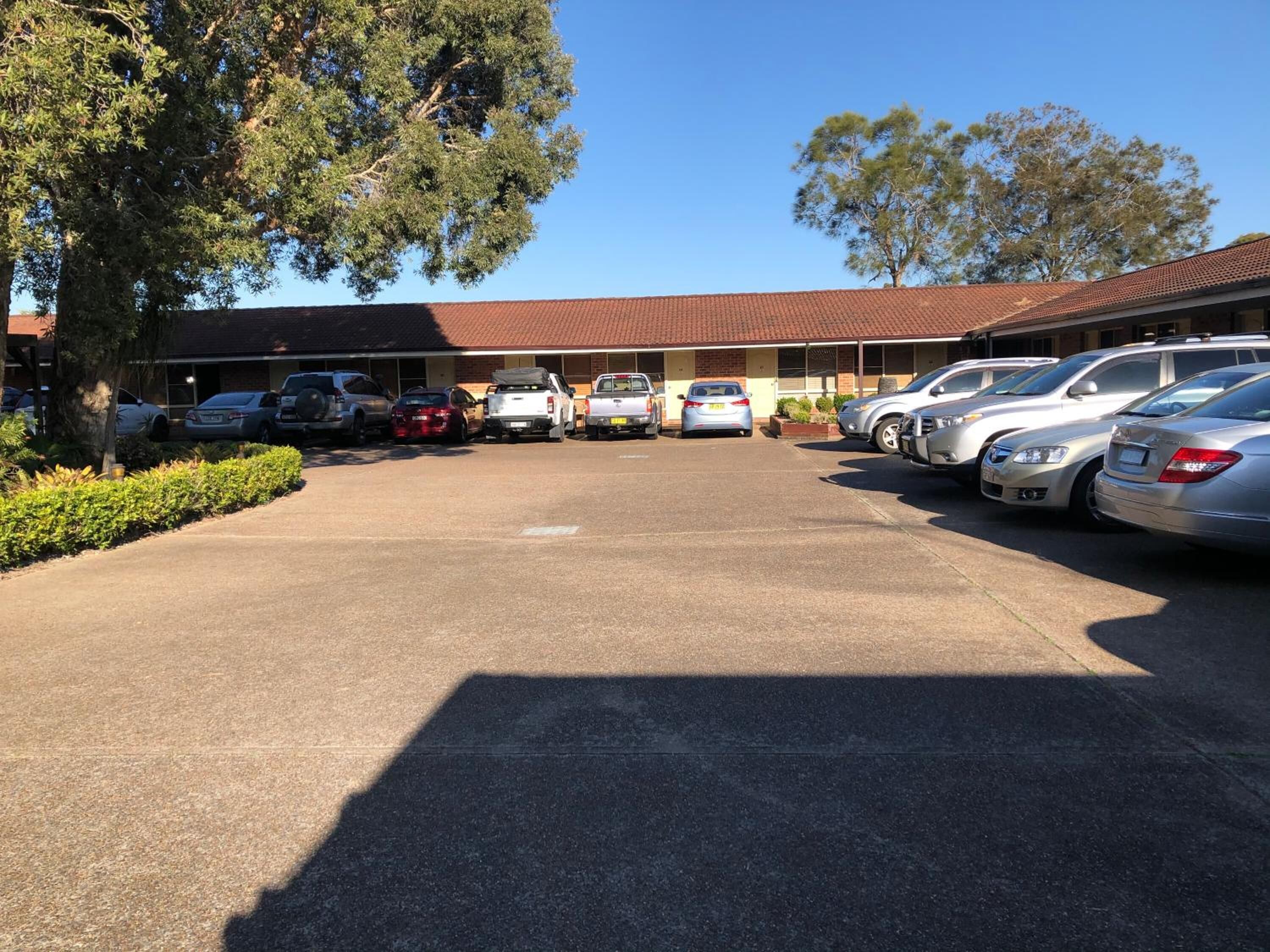 A parking lot with several cars parked in front of a building with a red-tiled roof.