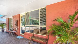 An outdoor seating area with a bench, chairs, and a potted plant. - Lake Macquarie Motor Inn (Marks Point)