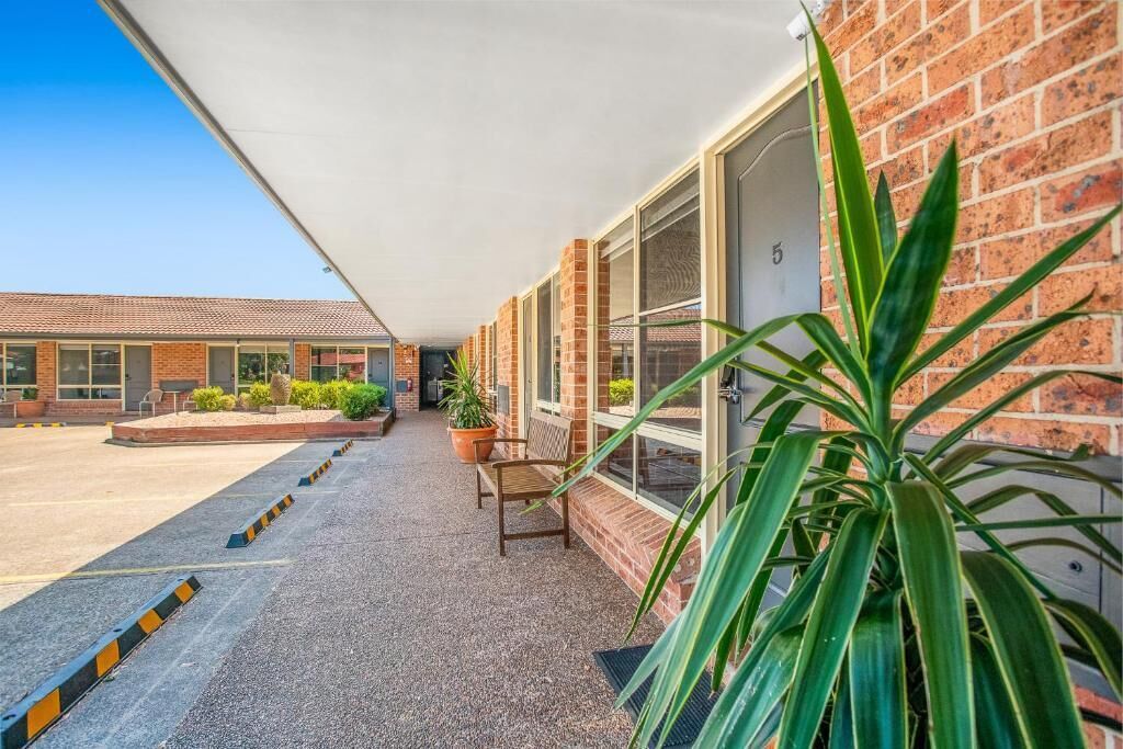 A motel with a covered walkway, potted plants, and a bench.