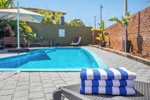 Una piscina al aire libre, sombrillas, sillones reclinables de piscina
