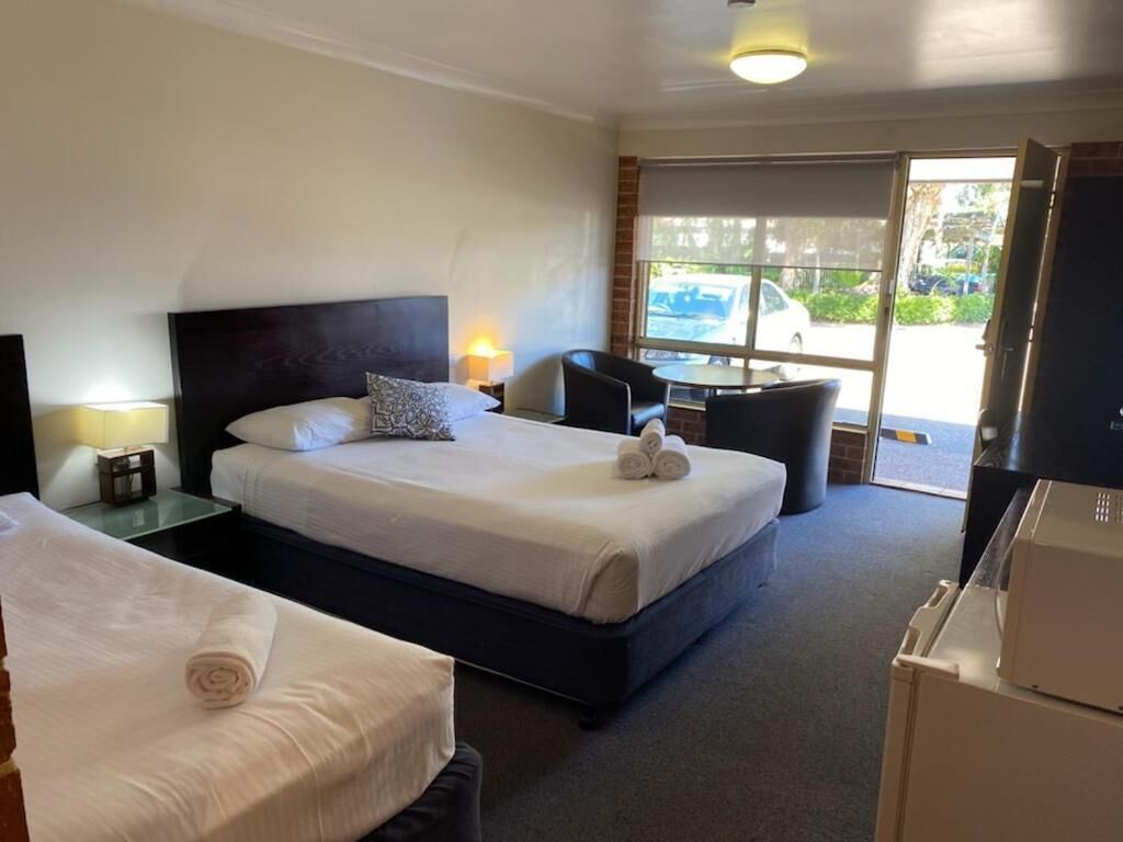A hotel room with two beds, a small table, a chair, and a view of the outside.
