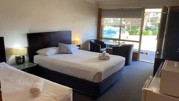 A hotel room with two beds, a small table, a chair, and a view of the outside.