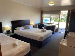 A hotel room with two beds, a small table, a chair, and a view of the outside. - Lake Macquarie Motor Inn (Marks Point)