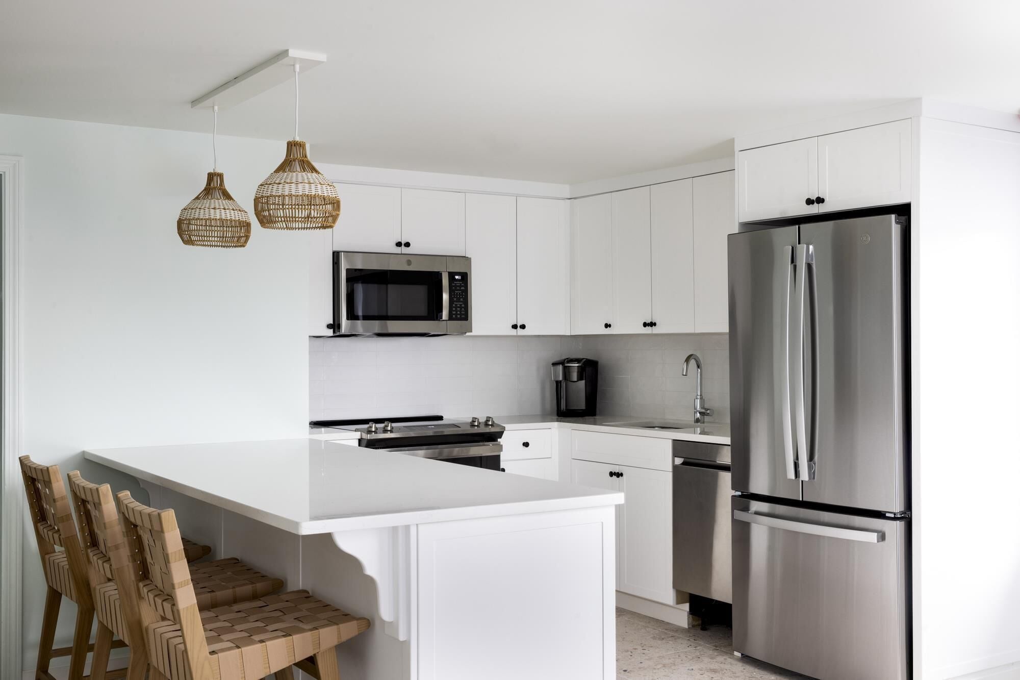 A modern kitchen with white cabinetry, a stainless steel refrigerator, a built-in oven, and a coffee maker.
