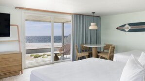 A hotel room with a bed, a desk, a chair, a table, and a view of the beach. - Riviera Beach Resort (South Yarmouth)