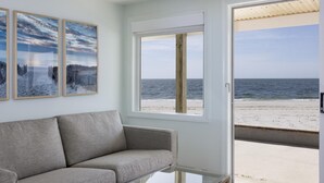 A room with a sofa, a glass coffee table, and a large window offering a view of the beach. - Riviera Beach Resort (South Yarmouth)