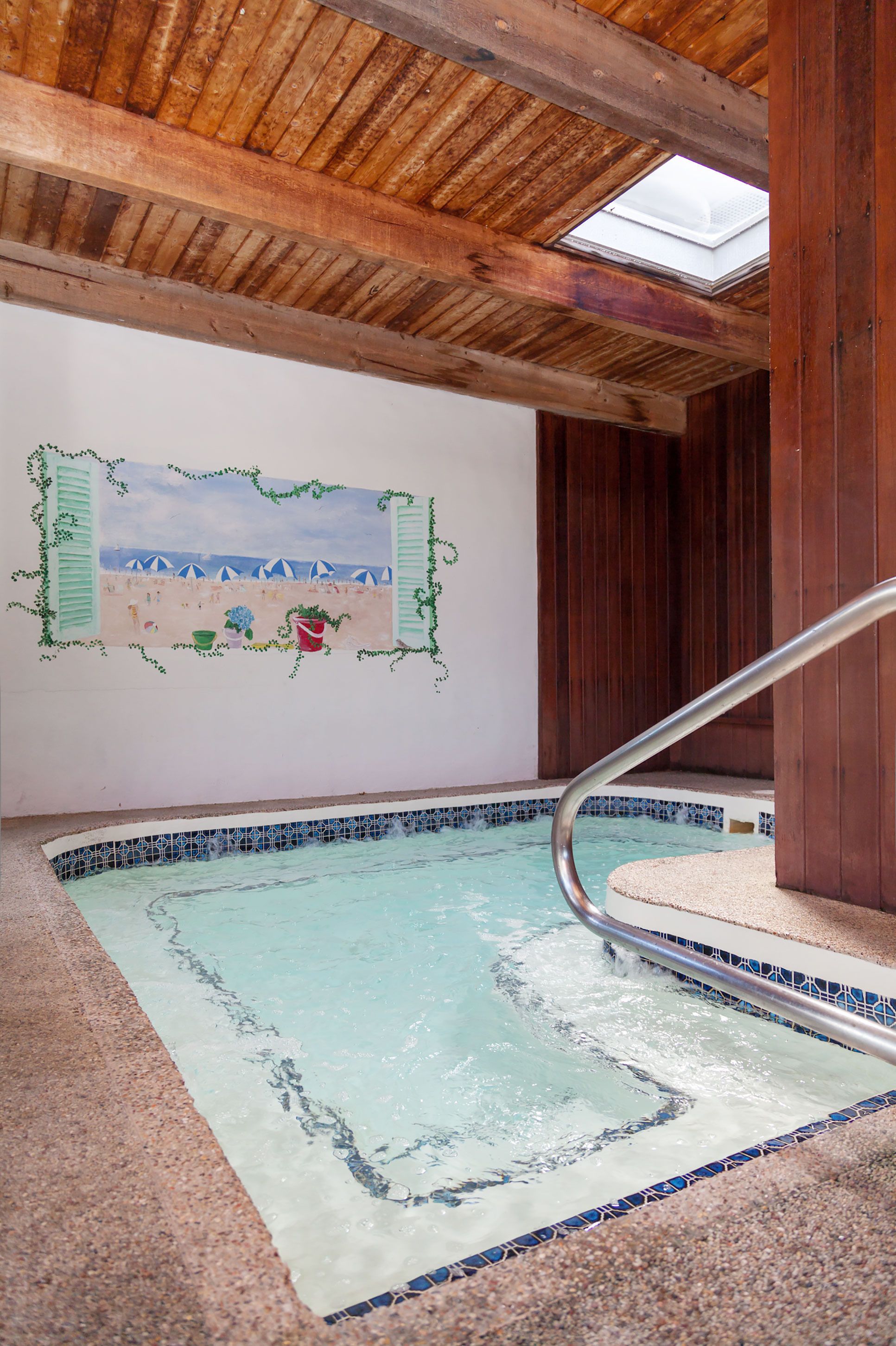 A swimming pool with a tiled edge, a wooden ceiling, and a wall mural.