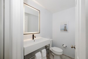 Un baño moderno con un lavamanos blanco, un espejo, un inodoro y un cuadro en la pared.