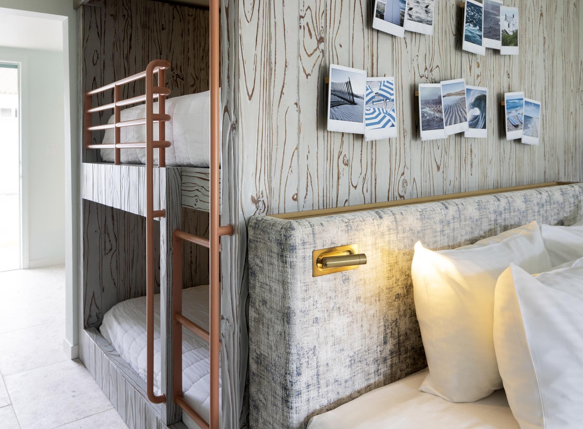 Une chambre avec un lit superposé, une échelle en bois, une tête de lit dotée d’un interrupteur et un mur décoré de photographies.
