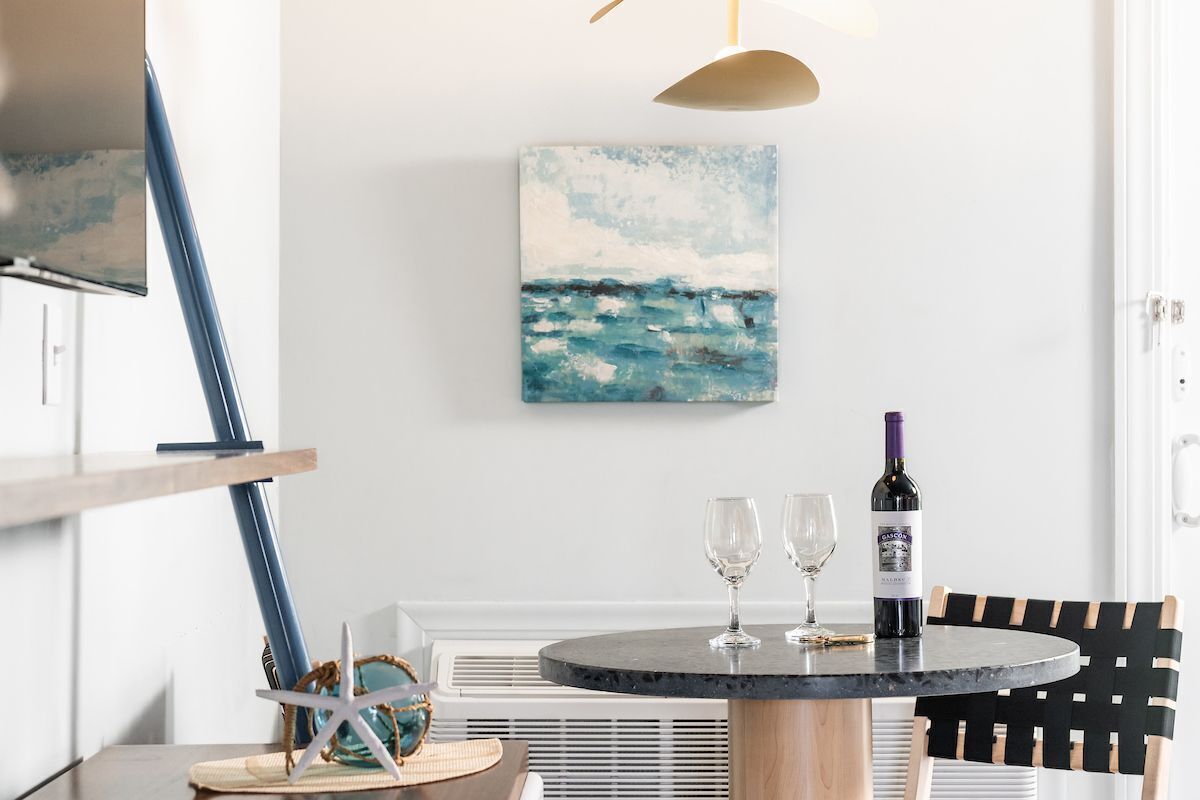 Een eetgedeelte met een ronde tafel, twee wijnglazen, een wijnfles, een zeester decoratie, en een schilderij van de oceaan aan de muur.