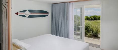 A bedroom with a bed, a view of the outdoors, and a surfboard decoration on the wall.