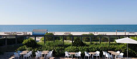A poolside area with a view of the sea, outdoor seating, and a clear sky.