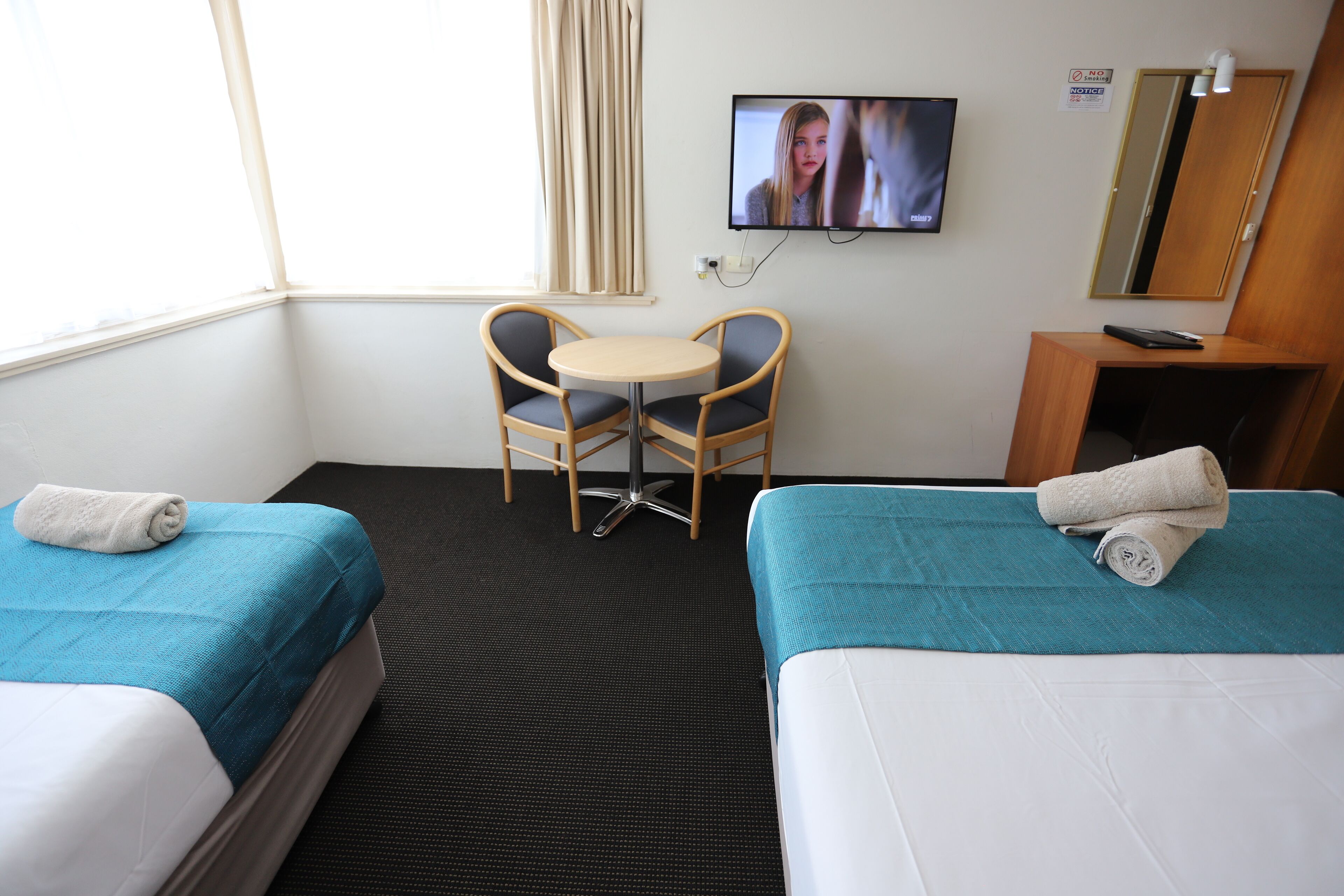 A hotel room with two beds, a small round table with chairs, a TV, a mirror, and a wooden cabinet.