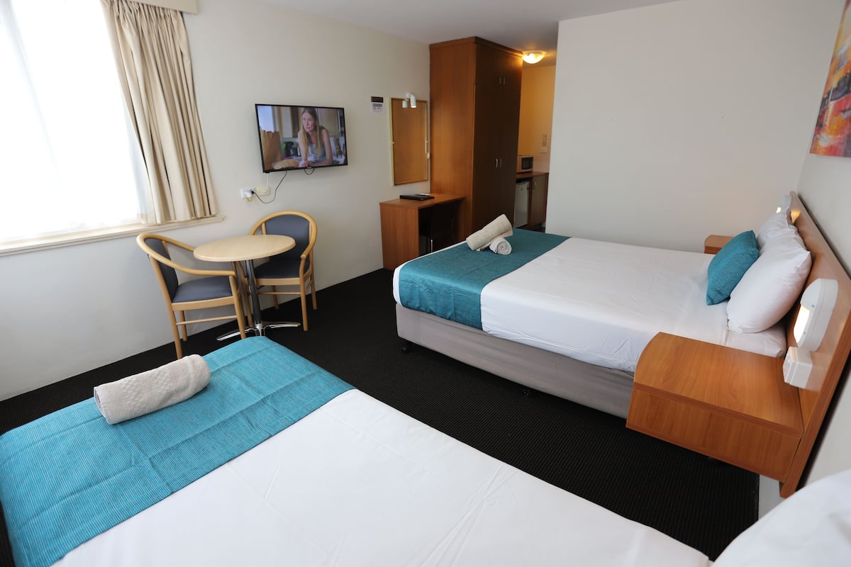 A hotel room with two beds, a desk, a chair, a television, and a small kitchenette.