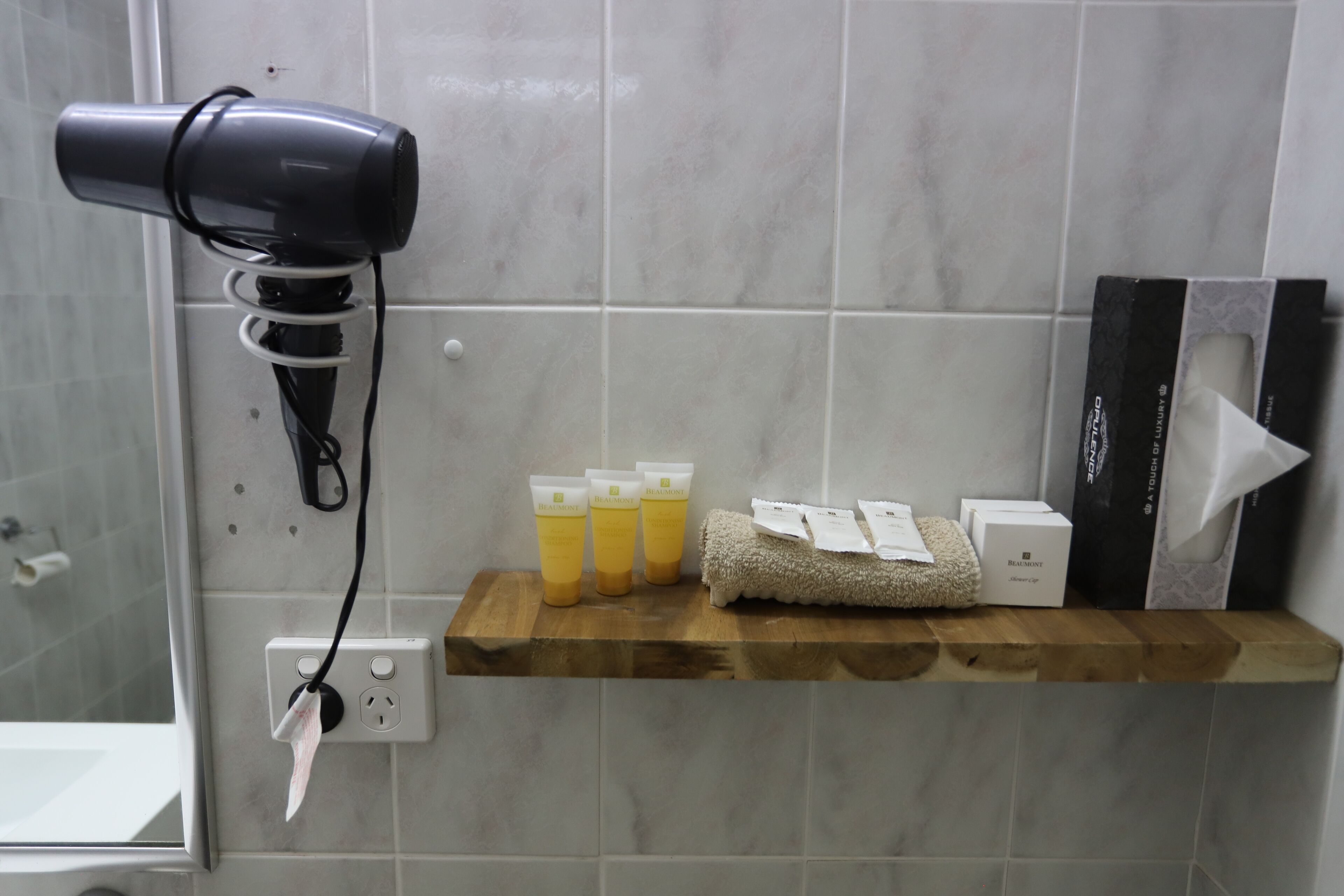 A bathroom with a hairdryer on a wall socket, a shelf with toiletries, and a towel.