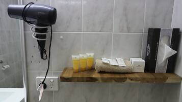 A bathroom with a hairdryer on a wall socket, a shelf with toiletries, and a towel.
