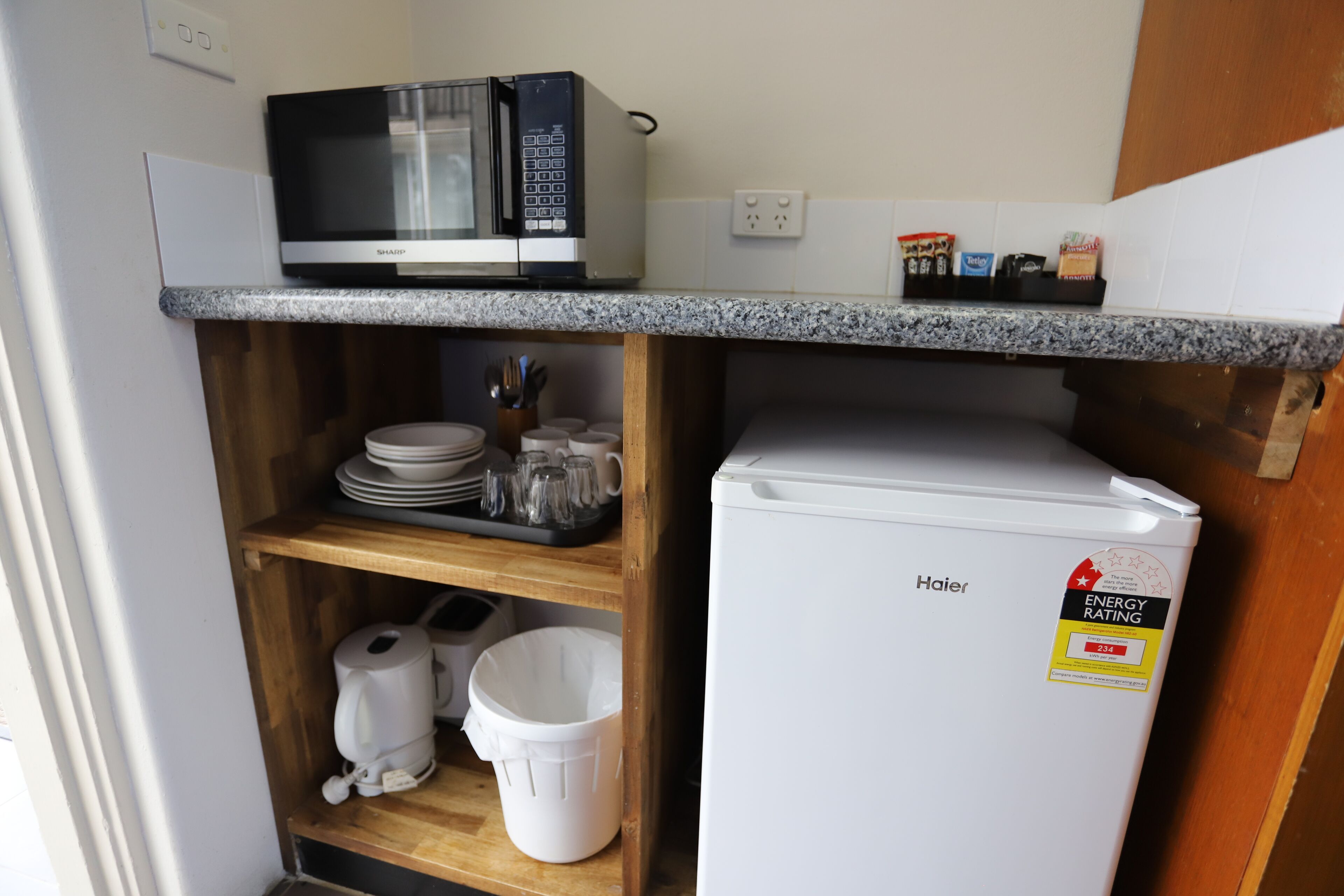A compact kitchen with a microwave, Haier refrigerator, and a countertop with kitchen essentials.