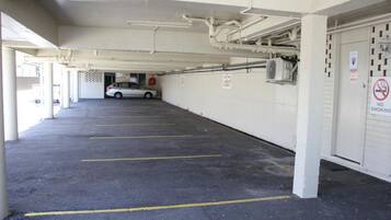 A parking garage with multiple parking spaces, a car in the distance, and a 'No Smoking' sign on the wall.