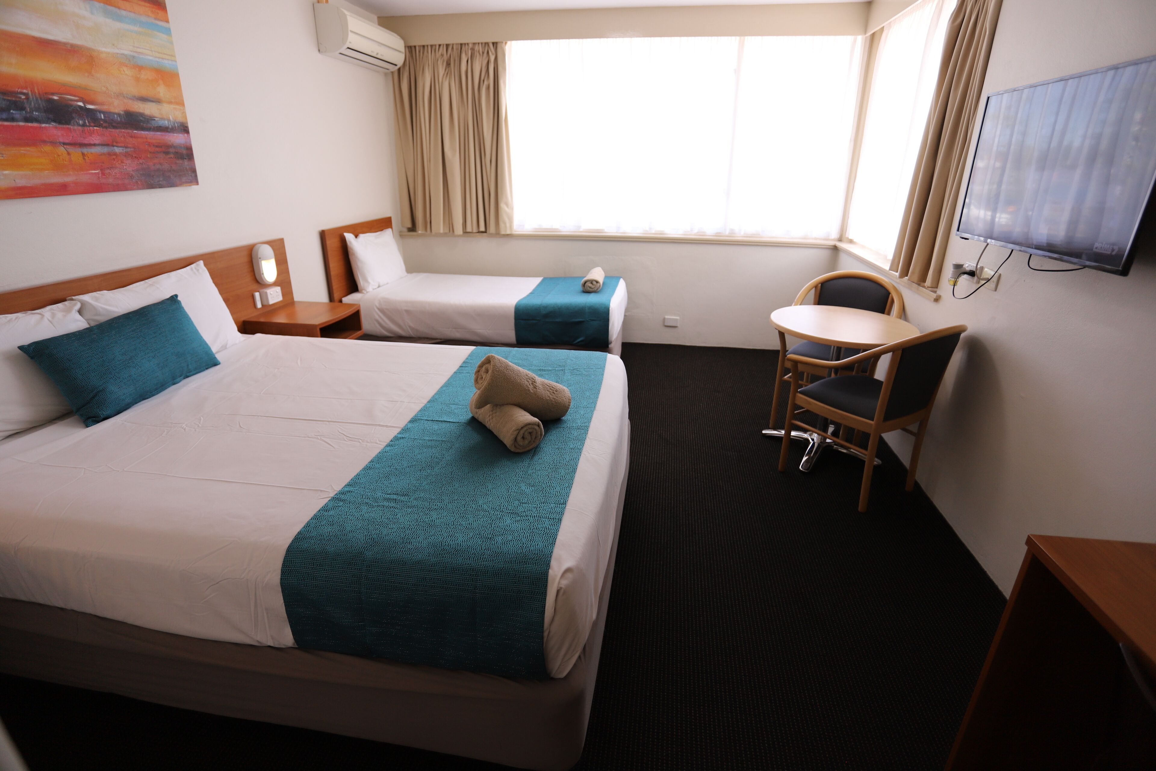 A hotel room with two beds, a desk, a chair, a TV, and a painting on the wall.