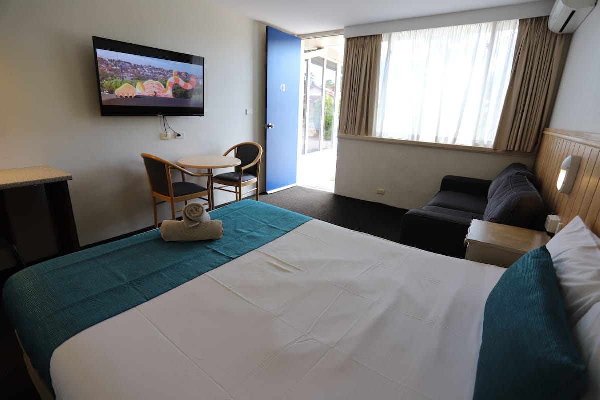 A hotel room with a bed, a desk, a chair, a TV, and a window with curtains.