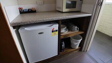 A compact kitchenette with a microwave, a small refrigerator, and a shelf with dishes and a kettle.