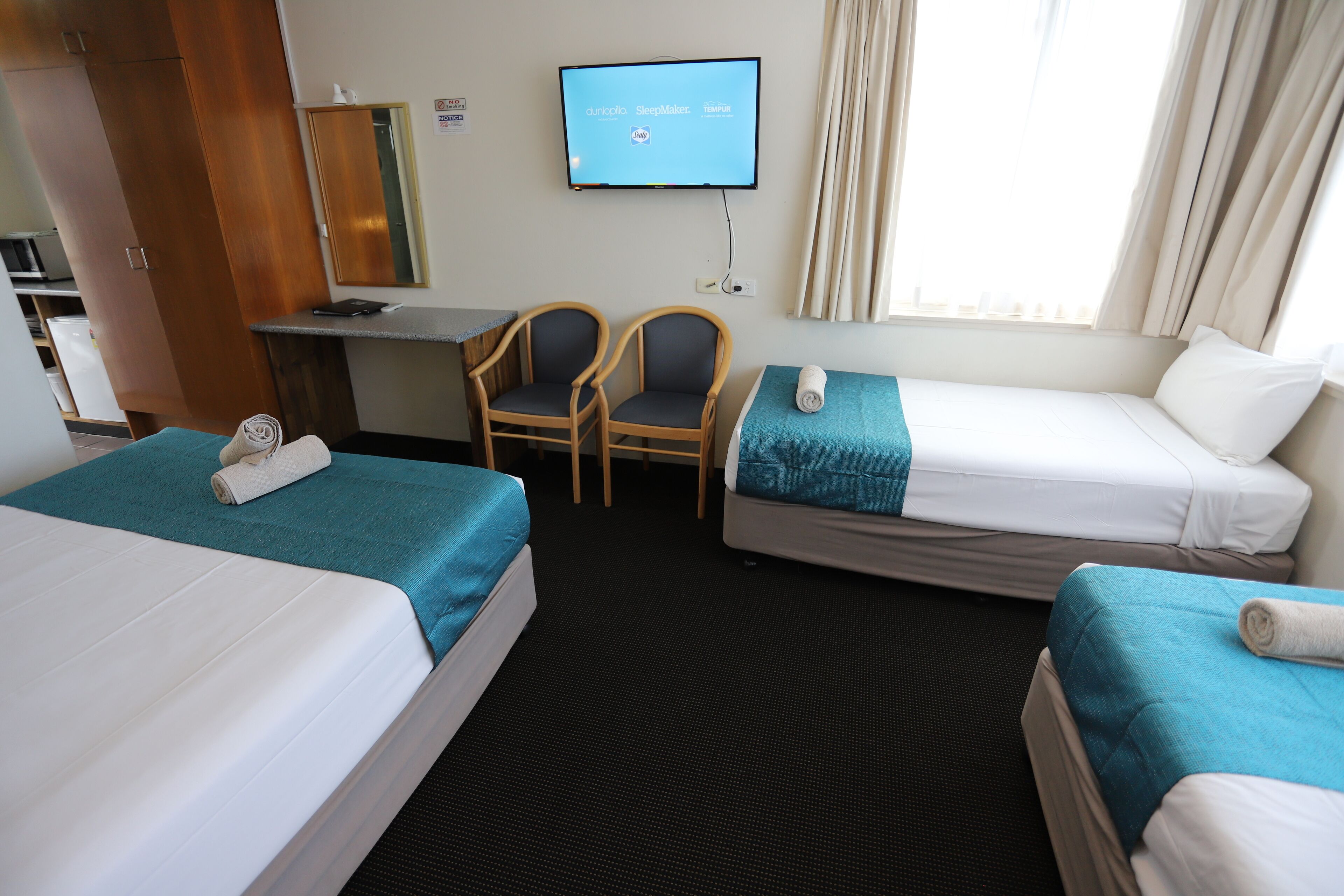 A hotel room with two beds, a desk, a chair, and a television on the wall.