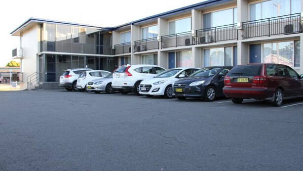En parkeringsplats med flera bilar parkerade framför en byggnad med flera våningar och balkonger.