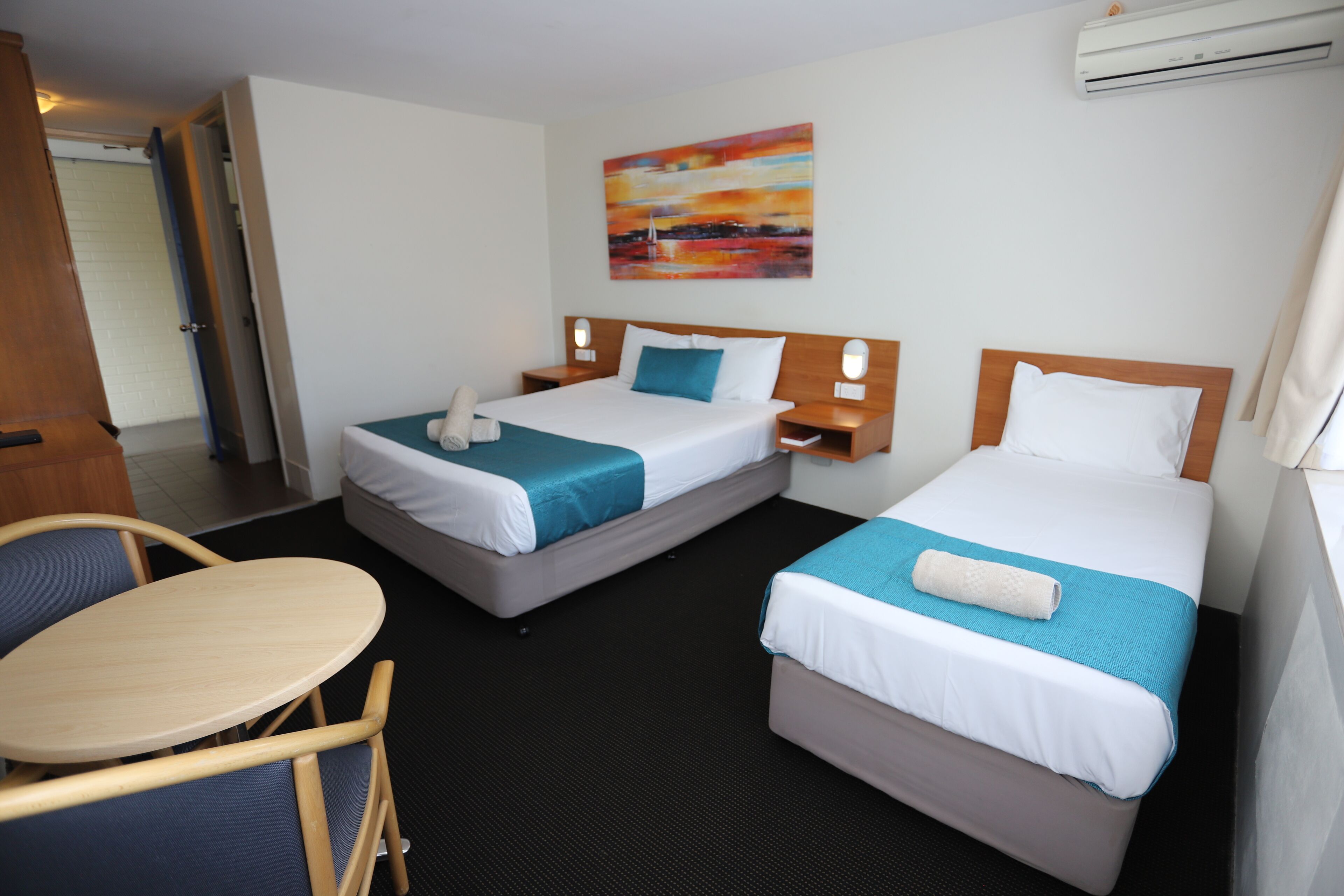 A hotel room with two beds, a small table, and a chair.