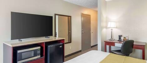Habitación de hotel con cama, escritorio con lámpara, microondas, refrigerador, televisor y puerta.
