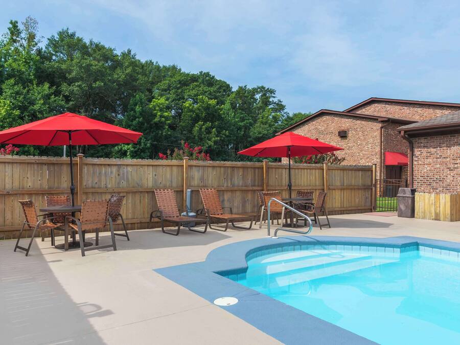 A backyard with a swimming pool, lounge chairs, and red umbrellas.
