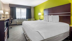 Ein Hotelzimmer mit einem großen Bett, einem Schreibtisch mit Lampe, einem Sessel und einem Fenster mit Vorhängen.
