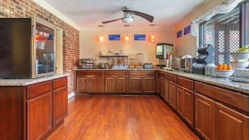 Une cuisine avec des meubles de rangement en bois, un réfrigérateur, un four à micro-ondes et un ventilateur de plafond.