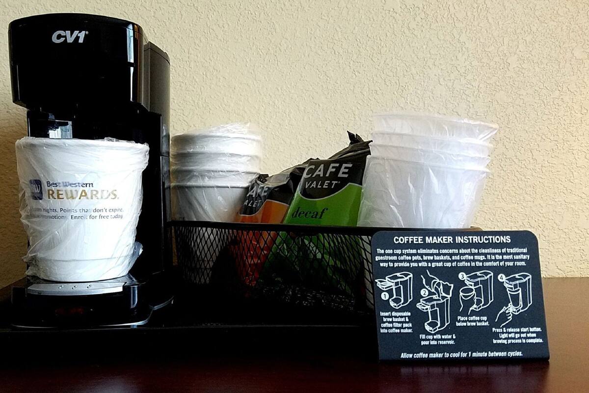 A coffee maker with disposable cups and a coffee maker instructions sign.
