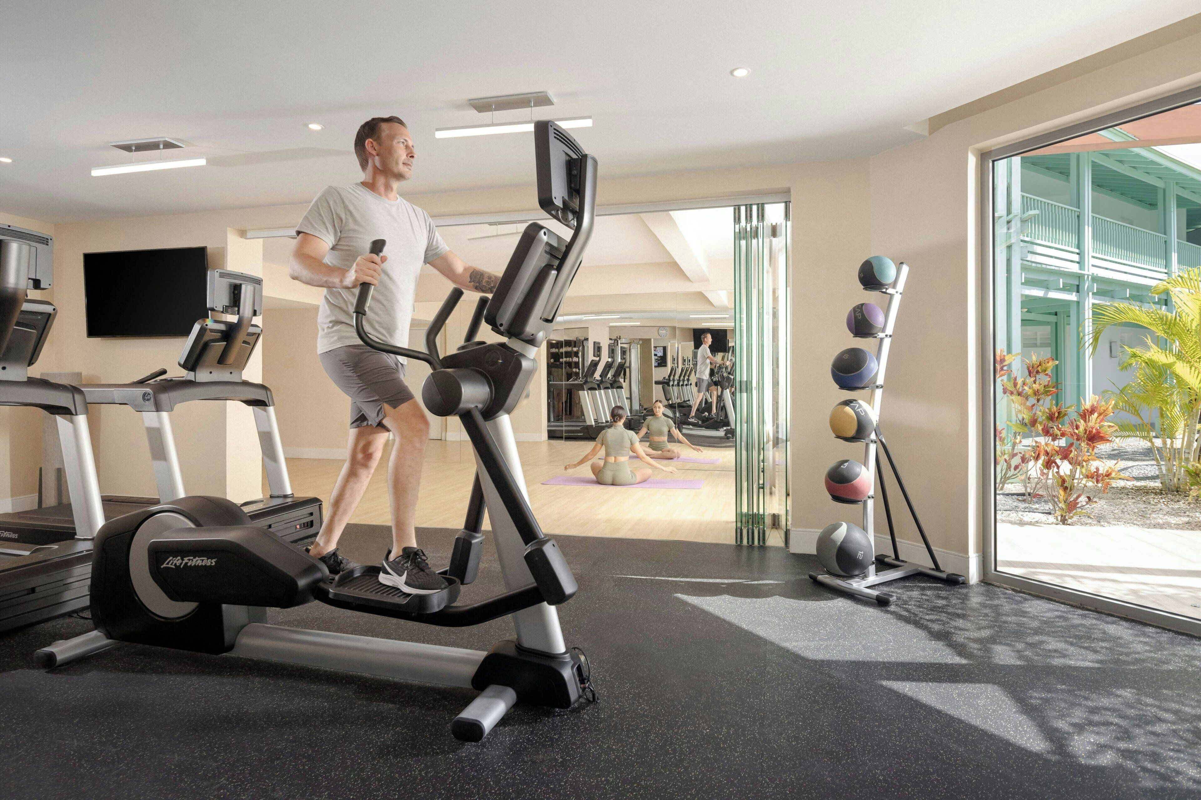 Een sportschool met cardioapparatuur, een yogamat gebied en fitnessballen.