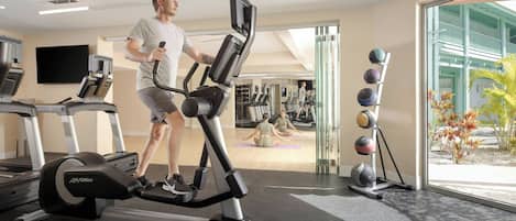 Un gimnasio con equipo de cardio, zona de colchonetas de yoga y pelotas de ejercicio.