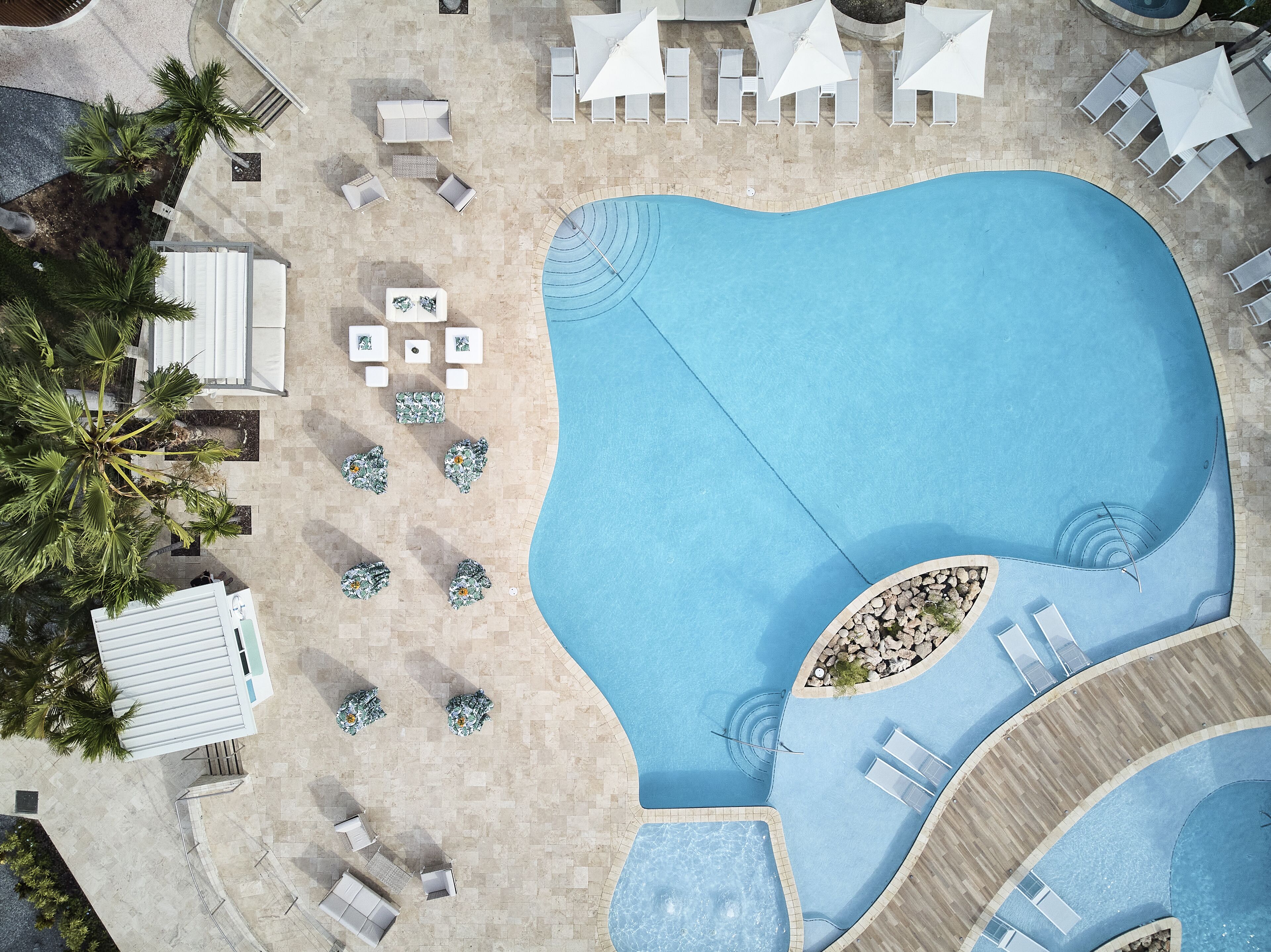 An aerial view of a swimming pool area with lounge chairs, a hot tub, and palm trees.