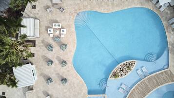 Vista aérea de un área de piscina con sillones de descanso, jacuzzi y palmeras.