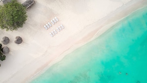 Vista aérea de una playa con arena blanca, agua turquesa cristalina y una fila de tumbonas blancas.