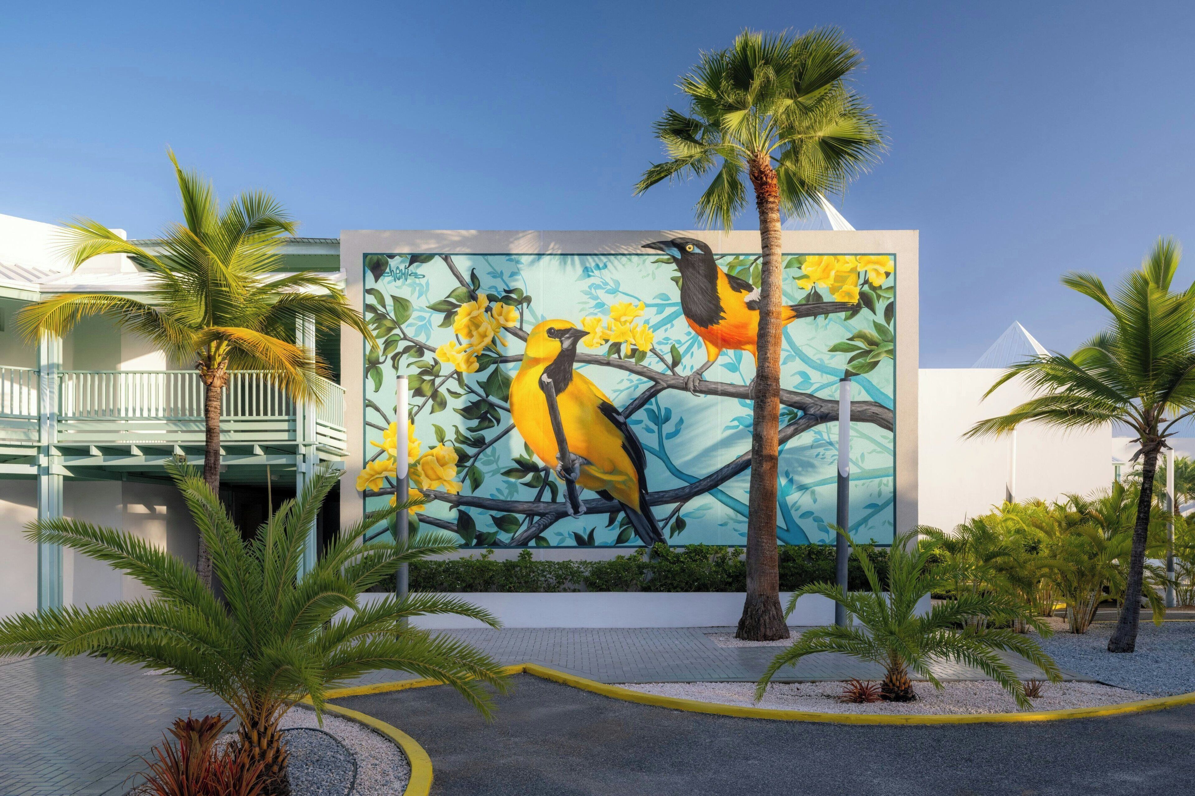 Une fresque représentant des oiseaux sur un bâtiment, des palmiers et un ciel dégagé.