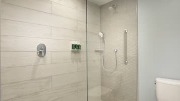 Un baño moderno con cabina de ducha de vidrio, un inodoro y una repisa con artículos de aseo.