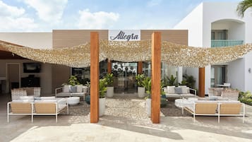 An outdoor seating area with a canopy, a sign reading "Allegra," and a modern building facade.