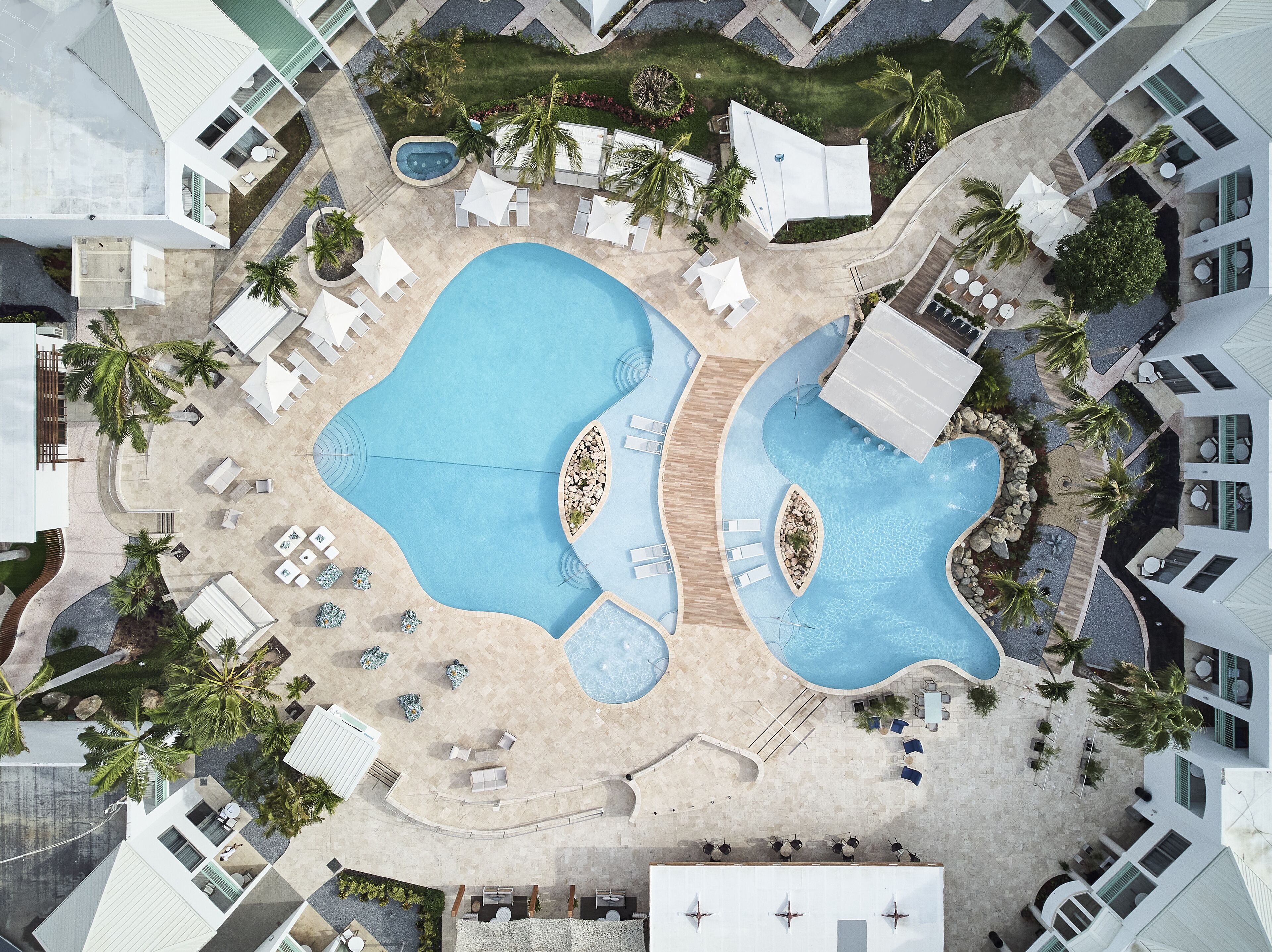 Vista aérea de un resort con múltiples piscinas, tumbonas y palmeras.