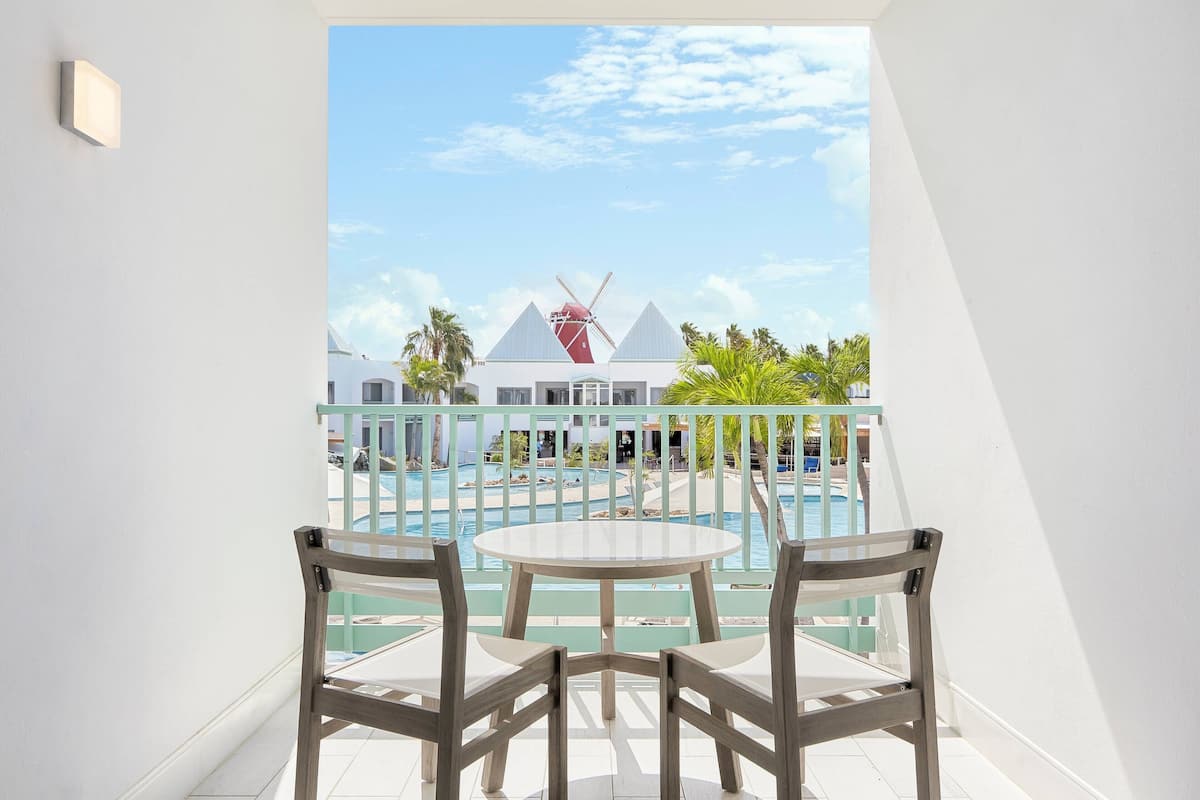 A balcony with a view of a windmill, pool, and resort buildings.