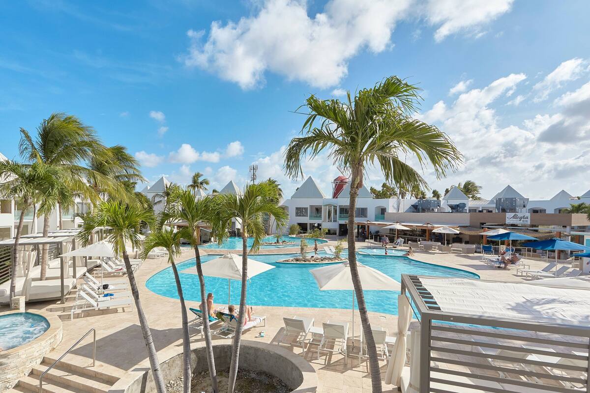 A resort pool area with multiple swimming pools, palm trees, and lounge chairs.