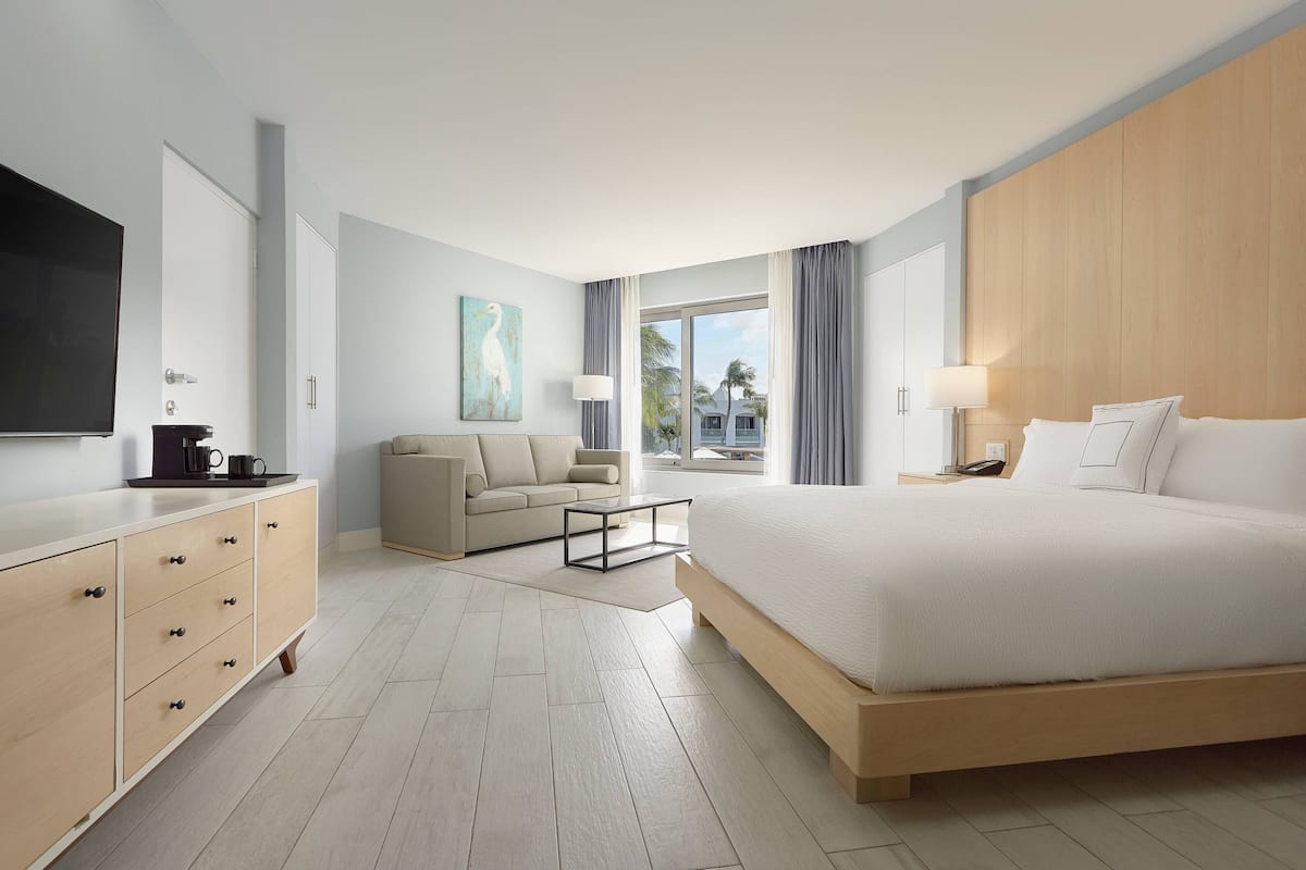 A modern hotel room with a large bed, a sofa, a coffee table, and a TV on the wall.